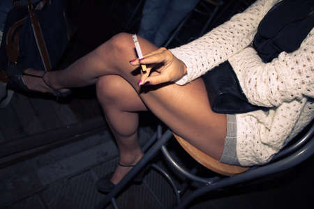 beautiful woman smoking a cigarette, young model smokes tobacco sitting on a chair (top view)の写真素材