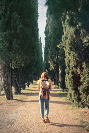 Traveler girl walking through cypress trees - Vertical picture of young woman with backpackの写真素材