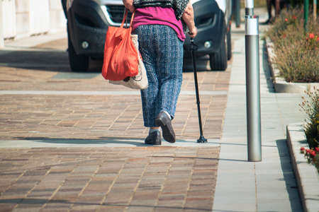walking stick detail, an old female person with bags walks using a support for deambulationの写真素材