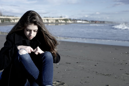 Sad teenager sitting in winter on the beach in front of the oceanの写真素材