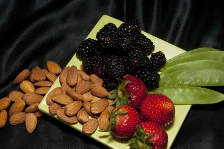 Berries, nuts, and snow pea pods on a light green plate against a black background are a healthy snack designed to refresh and keep fitの写真素材