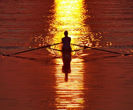 Lone crew rower strokes strongly in a shaft of early morning, red dawn sunlight on Lake Carnegie, Princeton, New Jerseyの写真素材