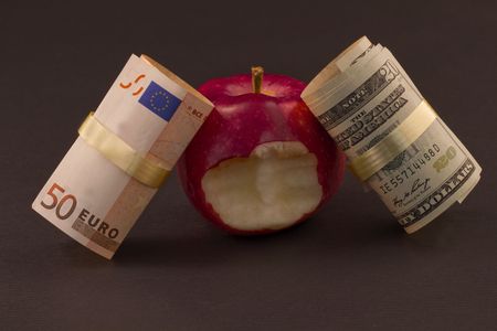 Two currencies, euro and dollar, lean against a red apple with a bite taken out of it, representative of economic struggles as well as personal financial issues within those connected economiesの写真素材
