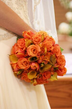 Bridal bouqet of orange roses and glimpse of an ivory wedding gownの写真素材
