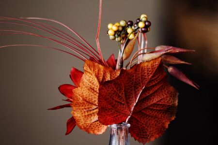 Auburn and orange leaves with berries in a small, tabletop vase capture the beauty of the season の写真素材