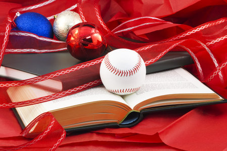 Baseball and books, open and closed, placed on red paper with holiday ornaments reflect the holiday fund raising support given to sports scholarships and scholars; の写真素材