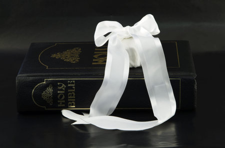 Large family Bible with white gift wrapped in white satin ribbon on simple, black background...