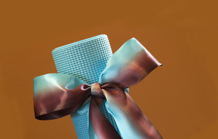 Blue yoga mat placed at an angle and tied like a gift with blue and tan satin ribbon against a tan...