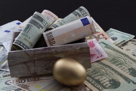 Rolled Euro and Dollar currency with gold nest egg on global currencies to depict worldwide emphasis on funding retirements and social network benefitsの写真素材