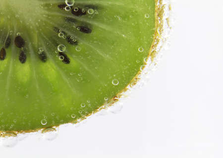 Kiwi fruit slice submerged in bubbling seltzer water creates a sense of energetic refreshment.の写真素材