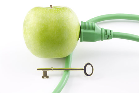 Golden key sits on electric cable with its plug inserted into green apple to represent the challenging key to a clean energy futureの写真素材
