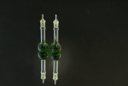 Two beakers with green fluid on mirror surface against black background with lighting highlight on...