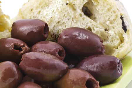 Greek Kalamata olives sit in front of a slice of kalamata bread on a light green plateの写真素材