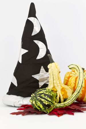 Wizard's hat with stars and moon placed behind decorative gourds on red, autumn leavesの写真素材