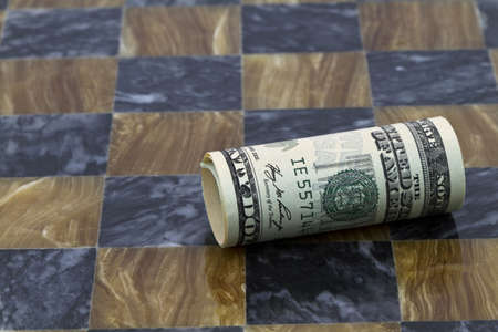 Dollar currency, rolled, lies on its side on chess board indicative of having fallen in struggle; dollar fallen in financial game; dollar's value fallen in game of life; の写真素材