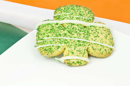 Cookie in shamrock shape on white plate placed on colors of Irish flagの写真素材