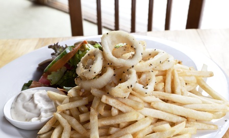 Platter of seasoned calamari with mayonnaise dip. Flakes of pepper visible on seafood placed on top of fried potatoes and accompanied by salad の写真素材