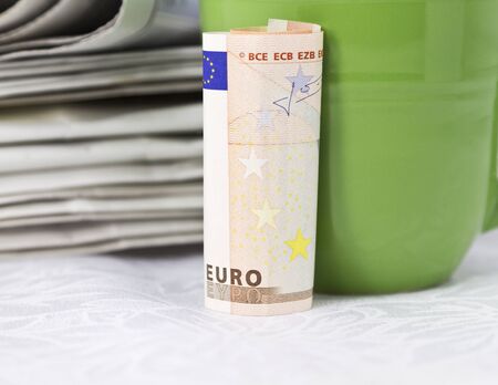 Euro currency with green mug placed in front of stack of newspapers; euro zone in the news; の写真素材