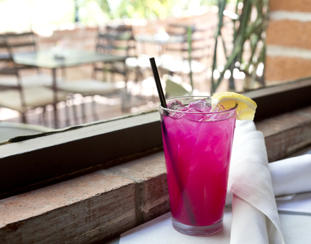 Pink lemonade with ice, lemon wedge, and black straw in tall glass by patio window with rustic,  brick sill. Location is Americaの写真素材
