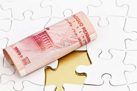 Chinese yuan on puzzle with missing piece. Business concept of finance shown with currency and gold beneath.の写真素材