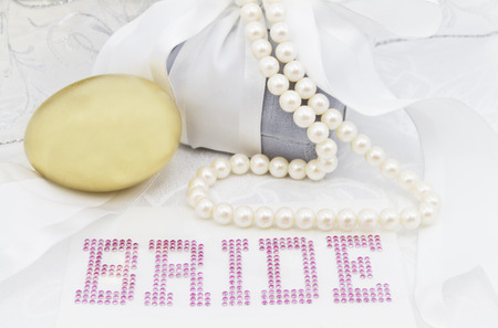 Feminine image of wedding day financial savings start.  Gold nest egg placed with BRIDE in pink letters surrounded by white ribbon, gray velvet gift box, and pearl necklace.の写真素材
