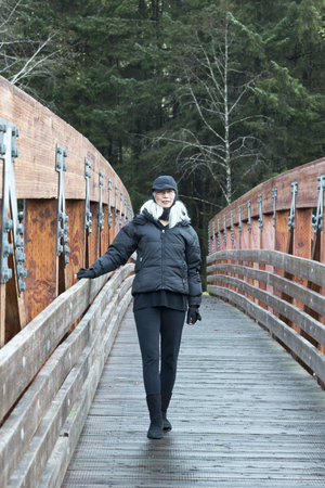 Asian senior woman in Juneau Alaska, on Fish Creek Trail, Douglas Island. Active senior bundled up in cold weather clothes for outdoor walking.のeditorial素材