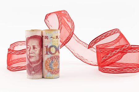 Yuan currency stands upright in front of swirl of red ribbon on white background in horizontal image.の写真素材