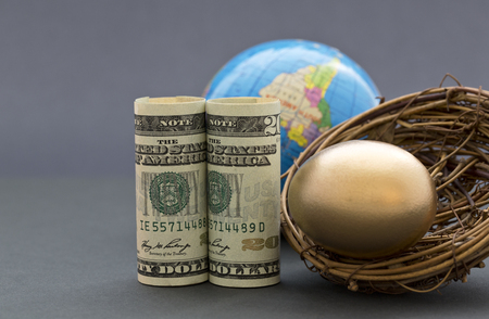 American dollars and gold nest egg with globe in sophisticated, gray background.  Success suggested by global investment and worldwide financial business. Selective focus on key, front metaphors.の写真素材