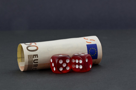 Pair of red dice in front of euro money placed on simple dark background depicts financial policies and business environments with chance and risk.の写真素材