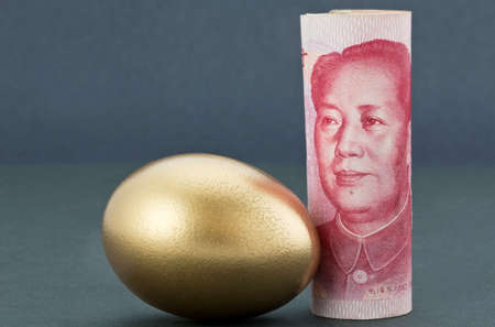 Chinese currency, Asian yuan, stands upright next to gold nest egg on soothing dark background reflects Pacific Rim strength and success in business and investment.の写真素材