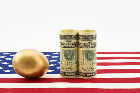 Gold nest egg with pair of American dollars placed on USA flag show success of national government policy and nation's business strength.  Horizontal image with copy space.の写真素材