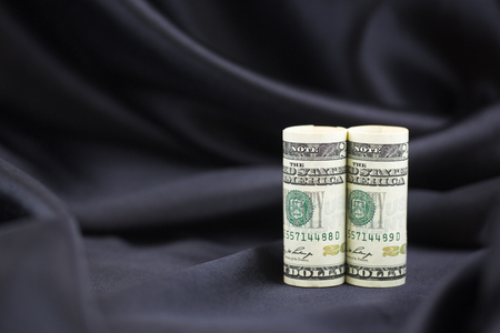 Pair of American dollars stand upright against elegant, simple black satin background reflecting power and success. の写真素材