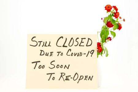 Bright red and orange lantana flowers accent a handwritten Too Soon to Reopen Covid 19 Sign