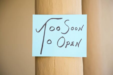 Blue paper, hand written announcement sign of Too Soon To Open attached to beige painted columnの写真素材