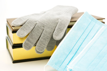 Gray winter gloves and books placed with Covid masks reflect essential Personal Protective...