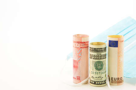 Global investments in health, medical, and pharmaceutical reflected in three currencies, yuan, dollar, and euro, next to medical protection masksの写真素材