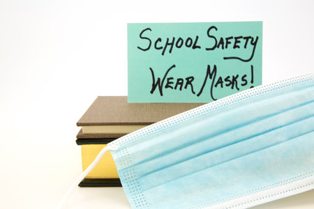 Blue card indicates SCHOOL SAFETY rule is WEAR MASKS.  Covid mask placed with books on white background.の写真素材