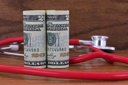 American money placed with red stethoscope on wood background reflects investment and costs in health care industries including nursing and physician education.の写真素材