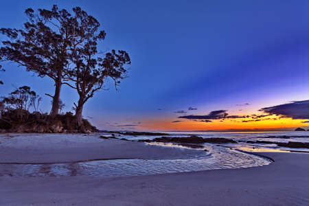 Adventure Bay in Tasmania, Australia, is bathed in the golden glow of sunrise on beach and waterの写真素材
