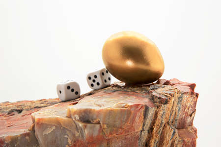 Gaming dice with gold nest egg on rock combine into symbolic warning to avoid financial risk to an investment nest eggの写真素材