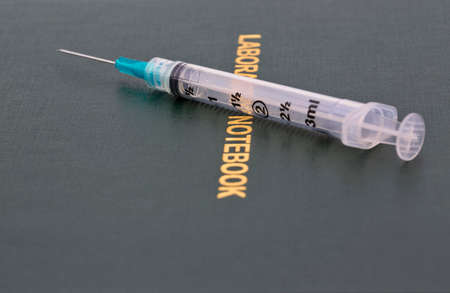 Injection needle placed on scientific Laboratory Notebook reflects that science and medicine are data-based in healthcare, pharmaceuticals, and medical industriesの写真素材