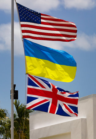 Flags of three nations, United States, Ukraine, and United Kingdom, on white flagpoleの写真素材