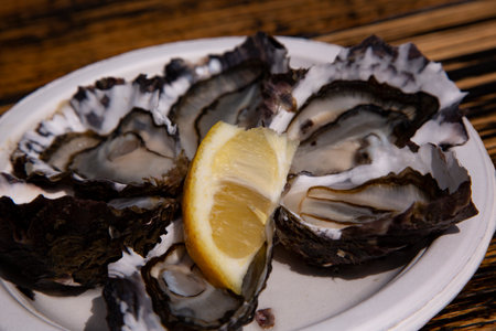 Freshly shucked oysters on the half shell with lemon slice on white platter on wood board tableの写真素材
