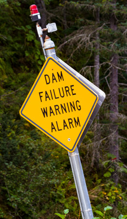 Badly tilted DAM FAILURE WARNING ALARM sign with red danger light in remote Valdez, Alaska, United Statesの写真素材