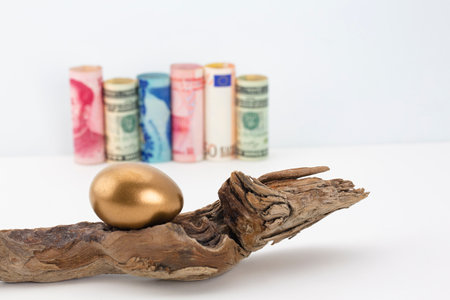 Global business success seen in gold egg symbol with diversity of national currencies, American and Canadian dollar, euro, and Chinese RMB n distant bokeh backgroundの写真素材