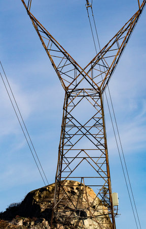 Vertical of electric power transmission lines supported by V shaped metal tower with sky and hill behind in British Columbia, Canadaの写真素材