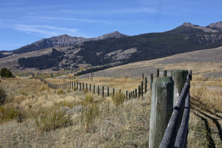 American West landscape of rolling fence line, Rocky Mountains, fields, and slopes along Tom Miner Creek Road, Gardiner, Montana, United Statesの写真素材