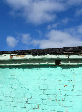 old green brick wall with pitched black roof on blue sky with white clouds, vintage construction detailsの写真素材