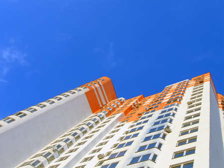 one new colorful orange building with many windows on blue sky with white clouds, new architecture detailsの写真素材