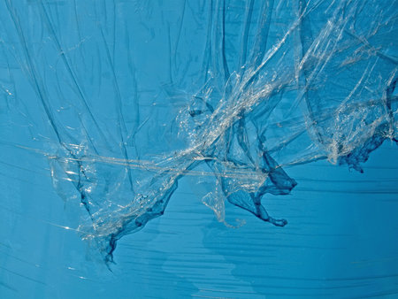 abstract transparent plastic oilskin pieces over blue surface, abandoned oil-cloth pieces
